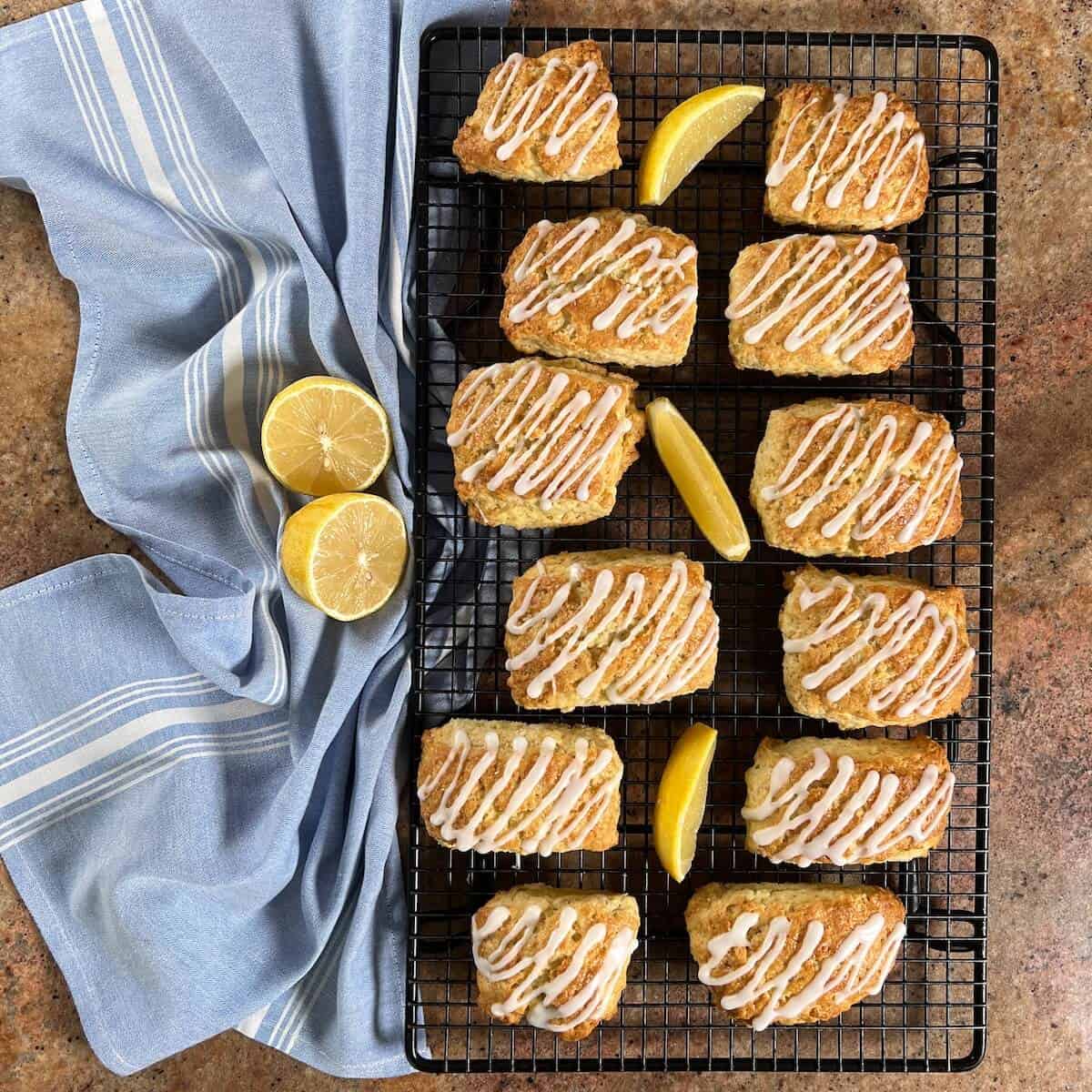 Glazed lemon scones on a cooling rack with lemon slices next to a blue towel.