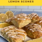 Lemon scones stacked on a white plate with lemon wedges all on a blue towel Pinterest banner.
