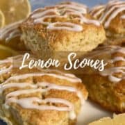 Lemon scones stacked on a white plate with lemon wedges all on a blue towel Pinterest banner.