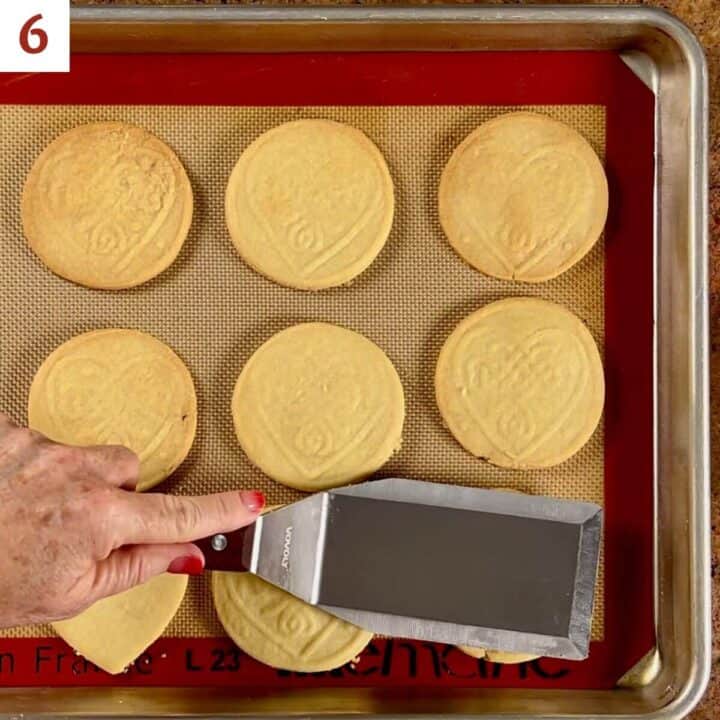 Flattening the puffed up areas of the baked shortbread cutout cookies with a spatula.