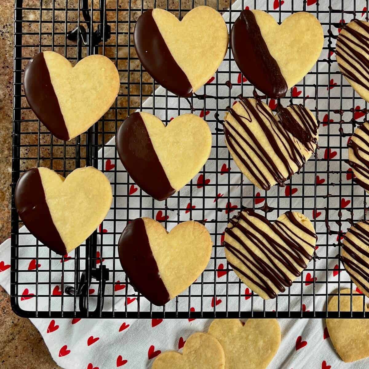 Heart shaped shortbread cutout cookies dipped or drizzled with chocolate on a wire rack.