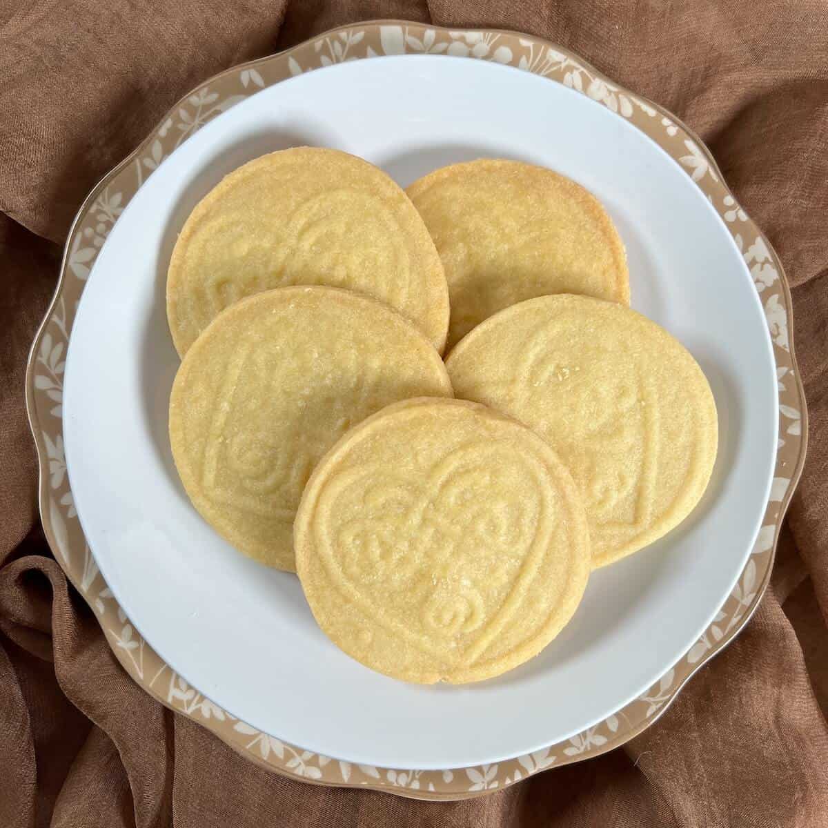 Round and stamped shortbread cutout cookies stacked on a white plate.