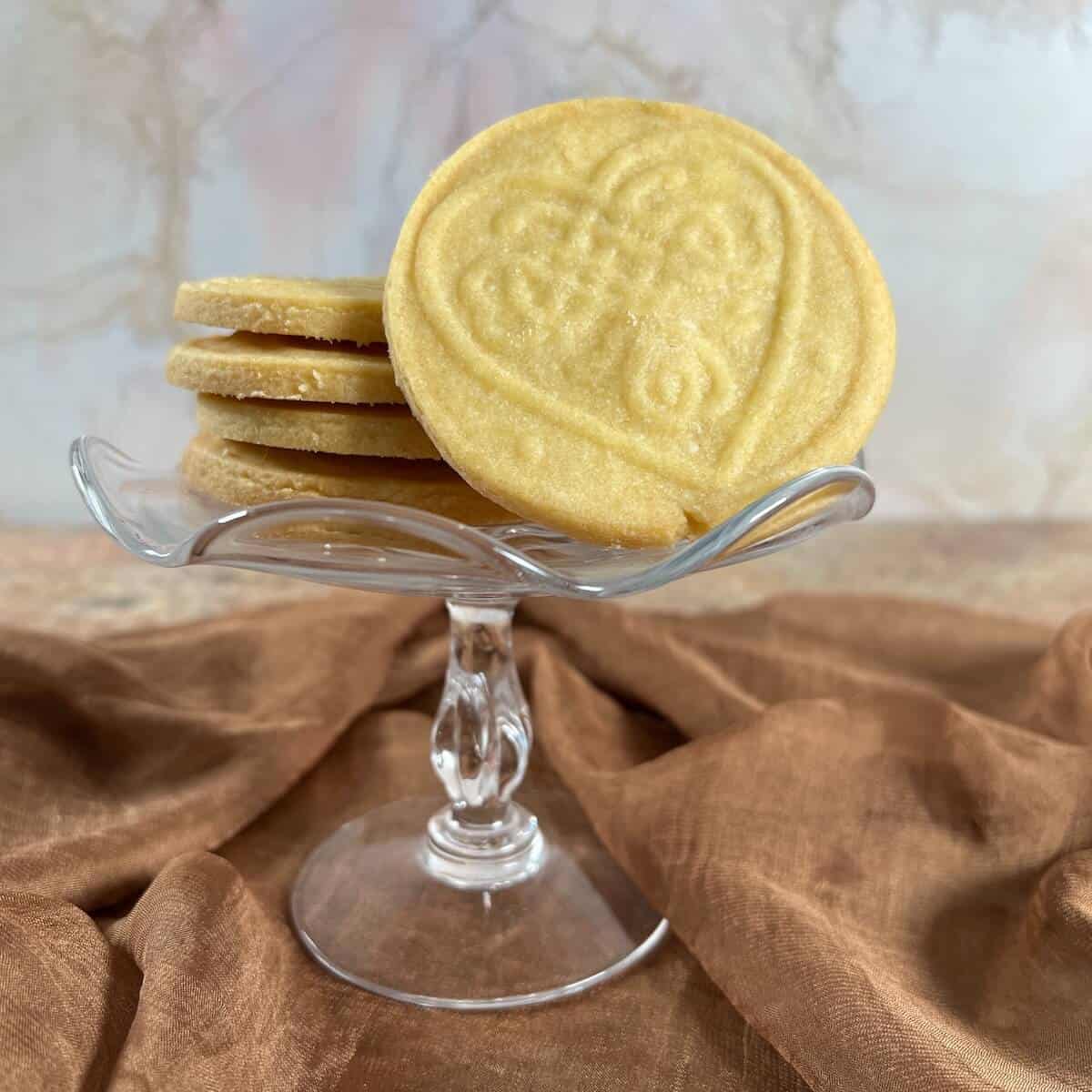Round and stamped shortbread cutout cookies stacked on a small cake stand with one showing design.