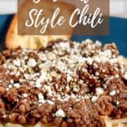 Cincinnati chili on a bowl of spaghetti topped with feta cheese with two pieces of garlic bread Pinterest banner.
