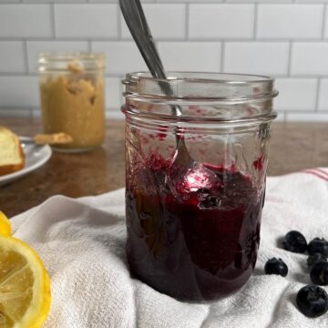 Mixed berry jam in a jar with a spoon inside in front of a jar of peanut butter.