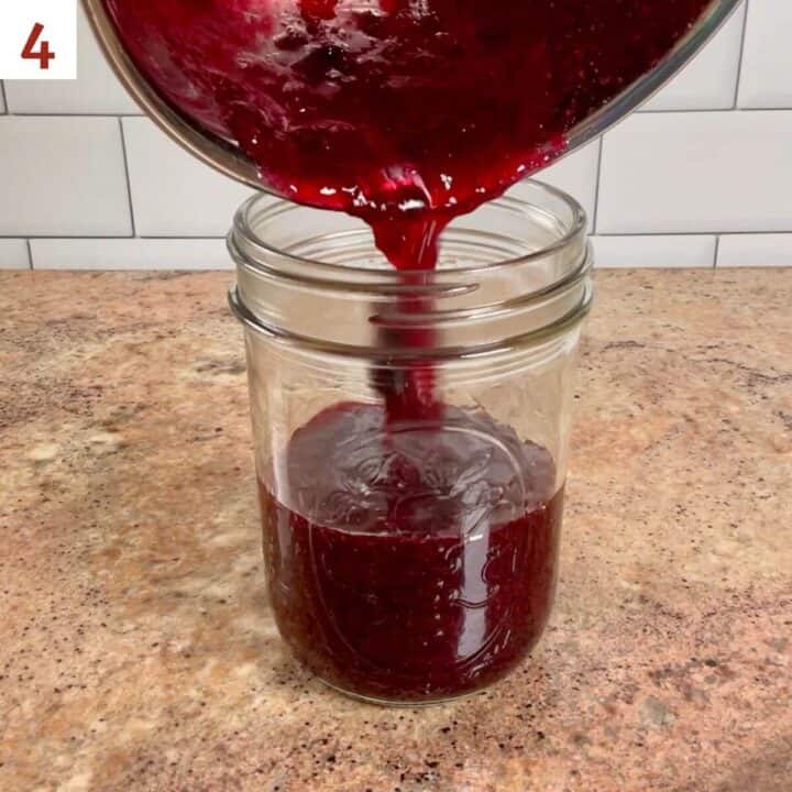 Pouring the finished mixed berry jam into a glass jar.