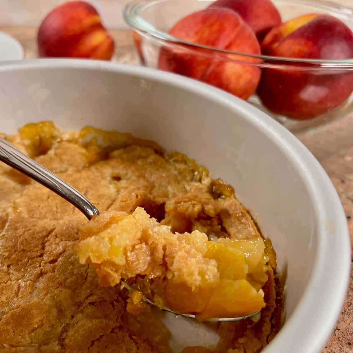Peach cobbler in a baking dish with a spoon lifting a bite.