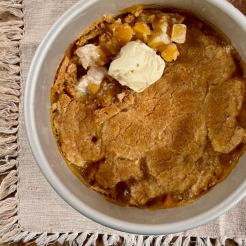 Peach Cobbler in a baking pan with a scoop of vanilla ice cream.