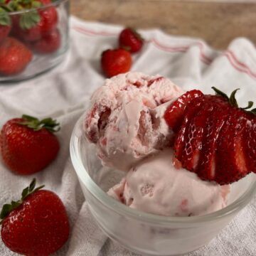 A bowl of strawberry ice cream with strawberries in a glass bowl.