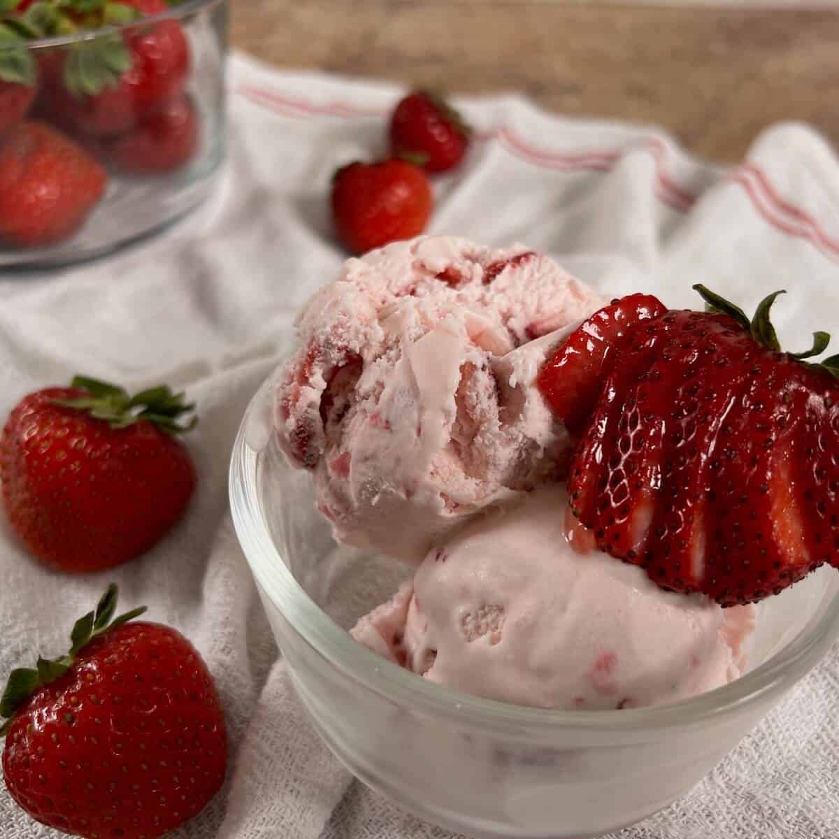 A bowl of strawberry ice cream with strawberries in a glass bowl.