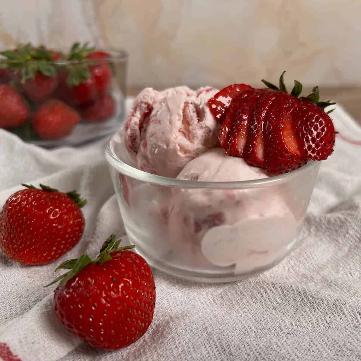 A bowl of strawberry ice cream with strawberries in a glass bowl.