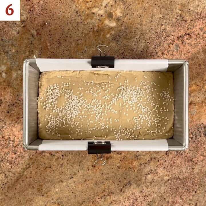 Tahini Halva in a loaf pan sprinkled with sesame seeds.