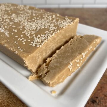Slice of Tahini Halva next to whole slab on a white plate.