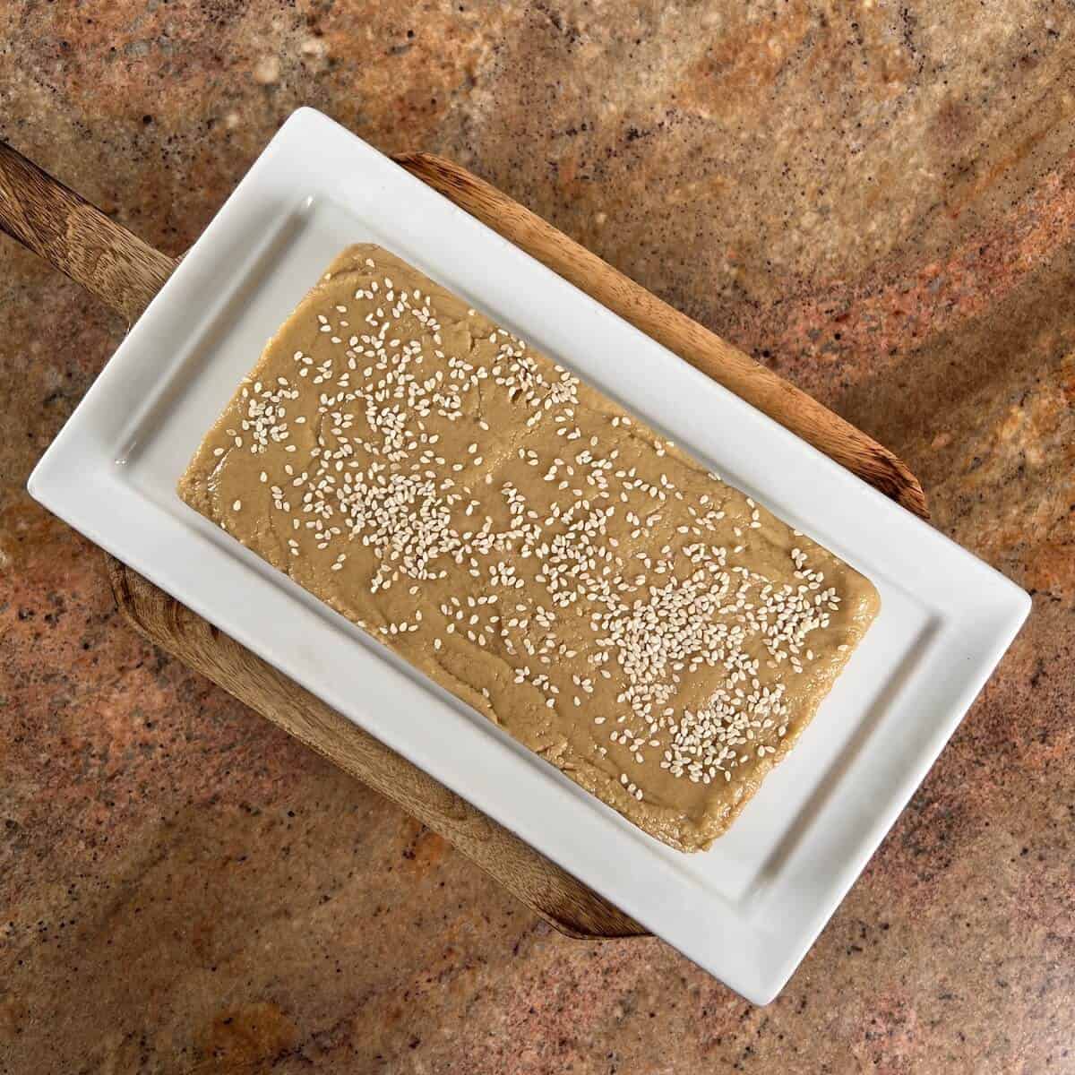 Whole Tahini Halva sprinkled with sesame seeds on a white platter.