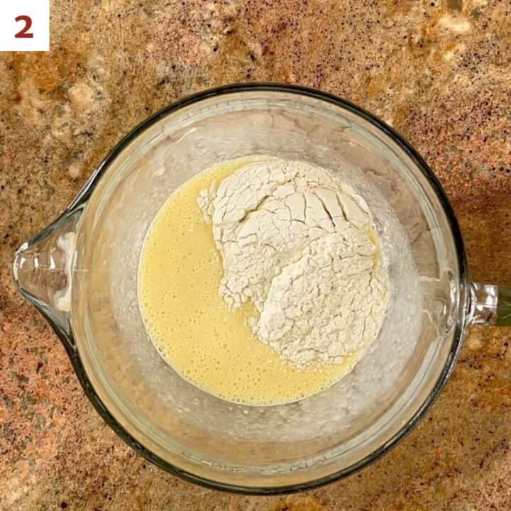 Adding flour to popover batter in a glass bowl.