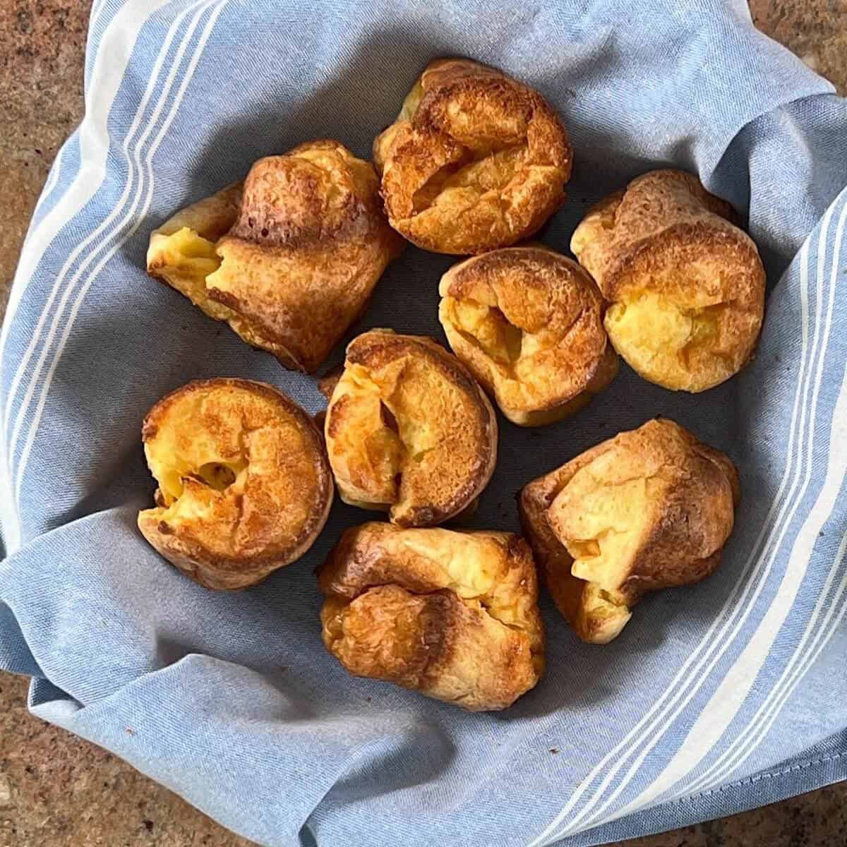 Eight Sourdough Discard Popovers in a bowl lined with a blue towel.