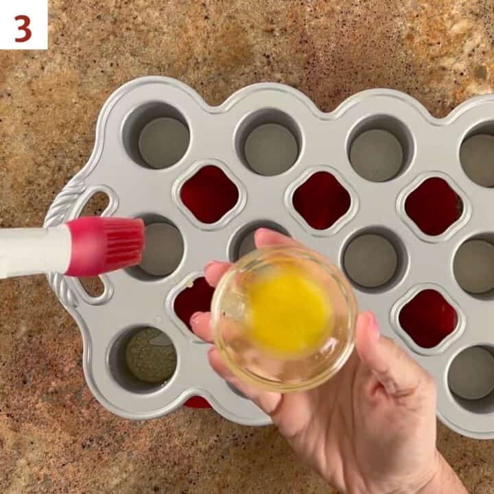 Brushing melted butter into the wells of a mini popover pan.