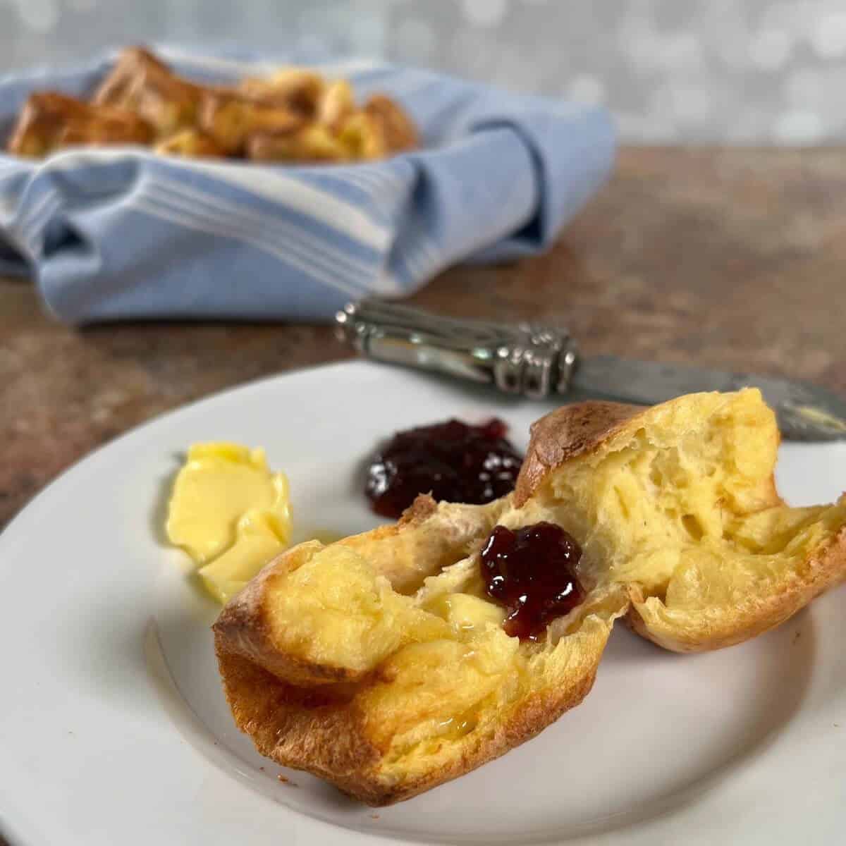 Sourdough Discard Popover on a white plate with butter and jam next to popovers in a blue bowl.