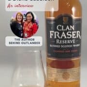 Bottle of Clan Fraser Reserve blended Scotch whisky beside a tasting glass, with an inset photo of Diana Gabaldon at New York Comic Con during an Outlander interview.