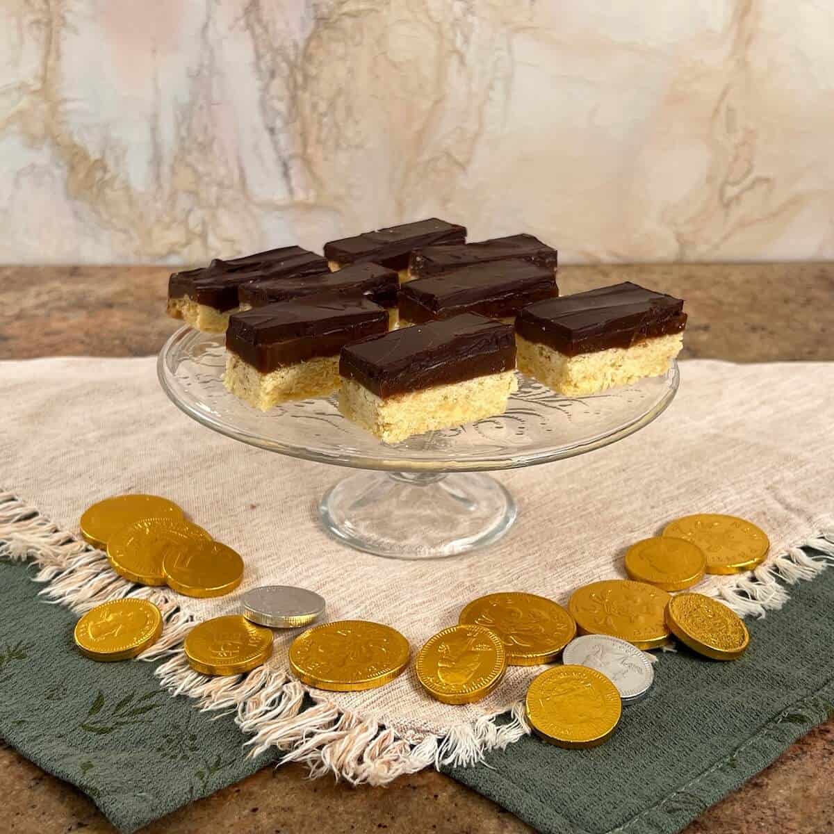 Millionaire's Shortbread on a glass cake stand with chocolate coins below.