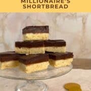 A stacked pile of Millionaire's Shortbread on a glass cake stand with chocolate coins below Pinterest banner.