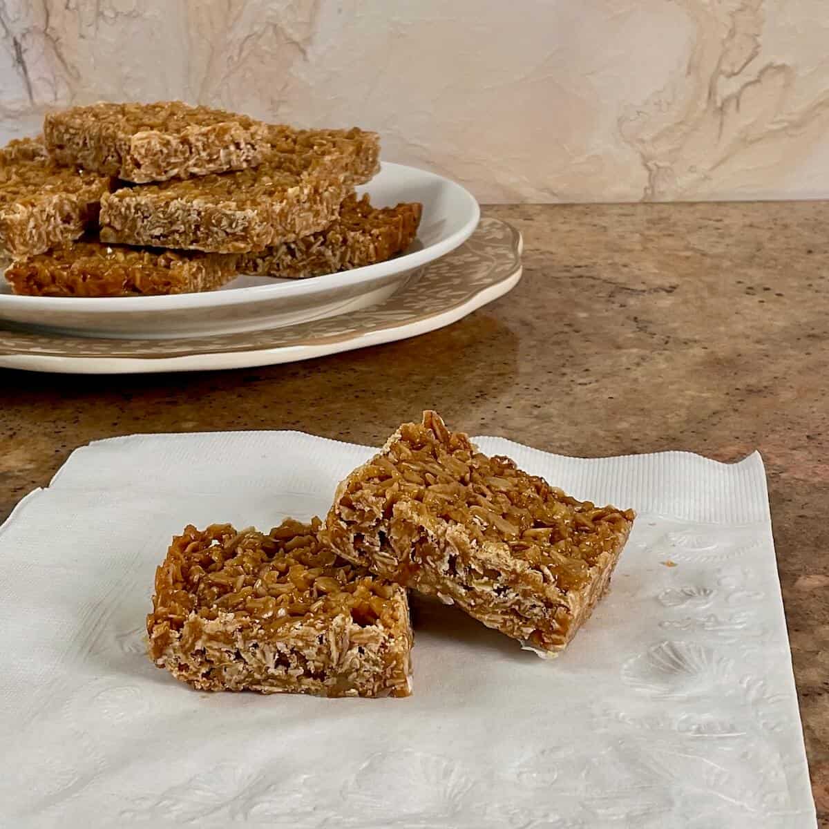 Two British flapjacks stacked on a white napkin with more stacked flapjacks plated behind.