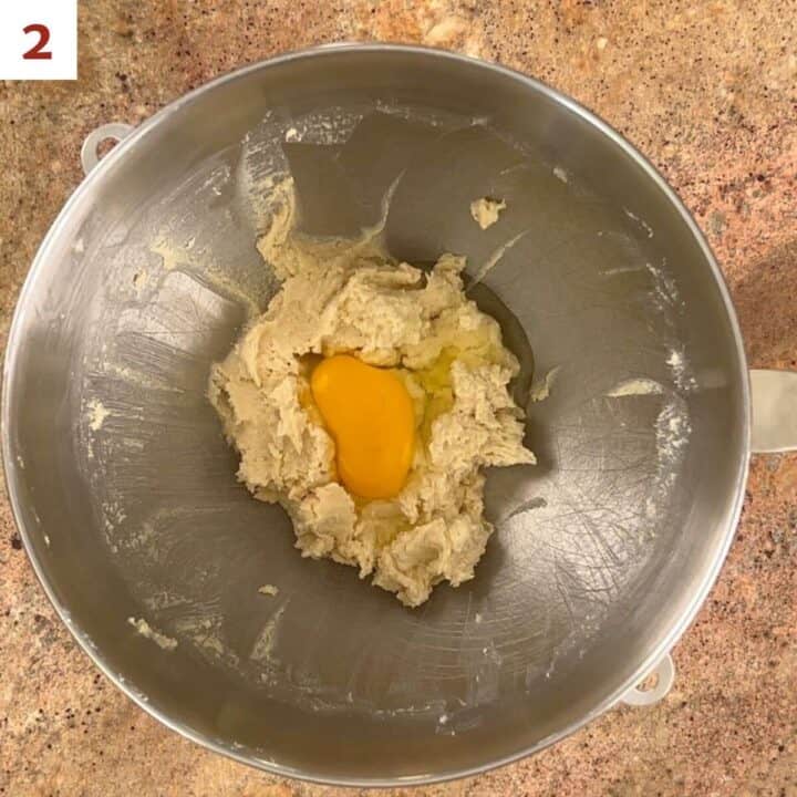 Adding the eggs to the cake batter in a metal mixing bowl.