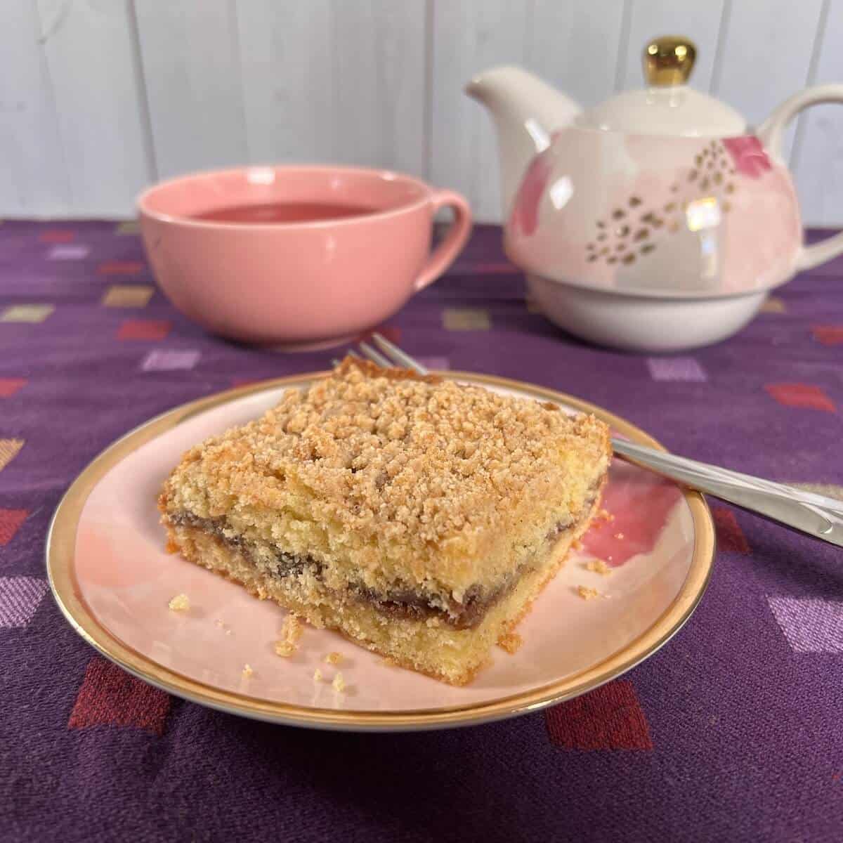Sourdough Discard Tahini Coffee Cake and a fork on a pink plate with a pink teacup and teapot behind it.