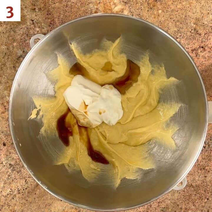 Adding sour cream, sesame oil, and vanila to cake batter in a metal mixing bowl.