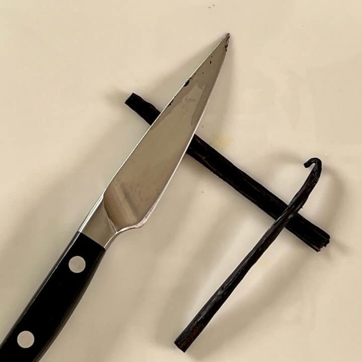 Split vanilla bean with a knife and cut bean all on a white plate.