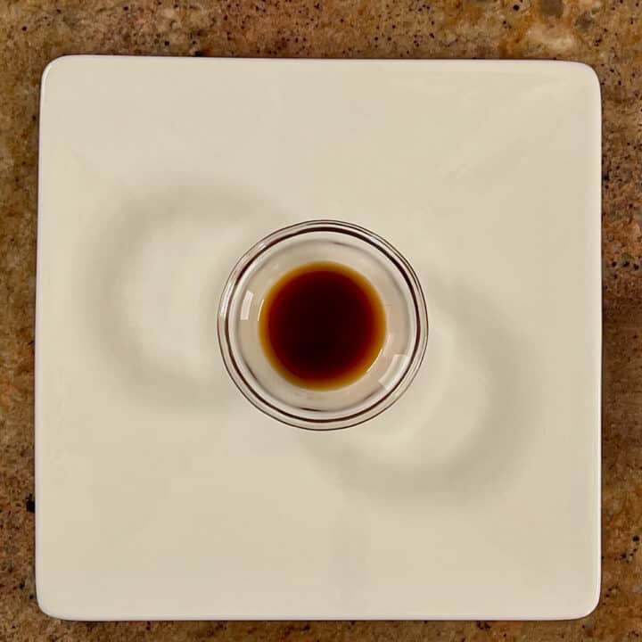 Vanilla extract in a glass bowl on a white plate.