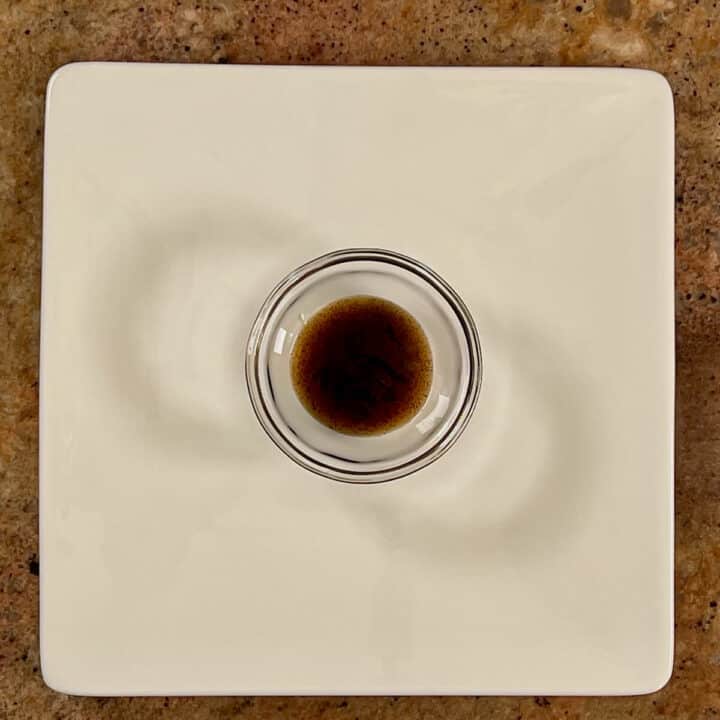 Vanilla bean paste in a glass bowl on a white plate.