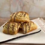 Vanilla Bean Scones stacked on a white plate with a vanilla bean in front.