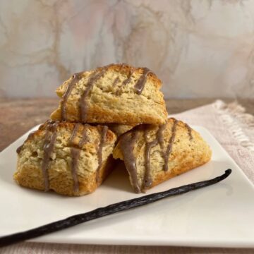 Vanilla Bean Scones stacked on a white plate with a vanilla bean in front.