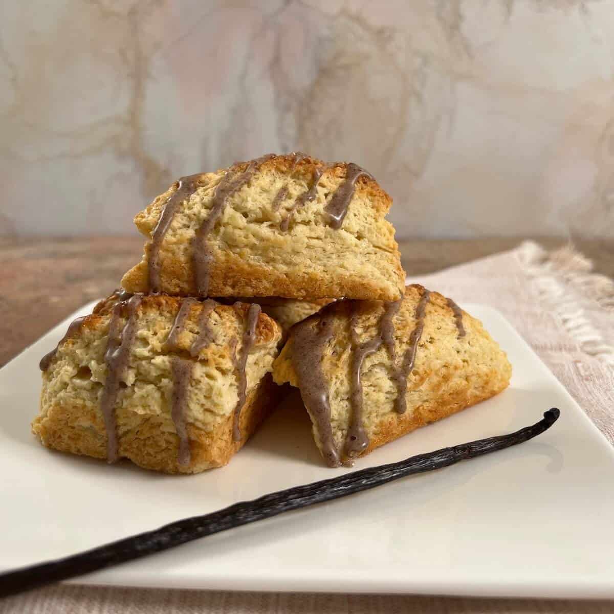 Vanilla Bean Scones stacked on a white plate with a vanilla bean in front.