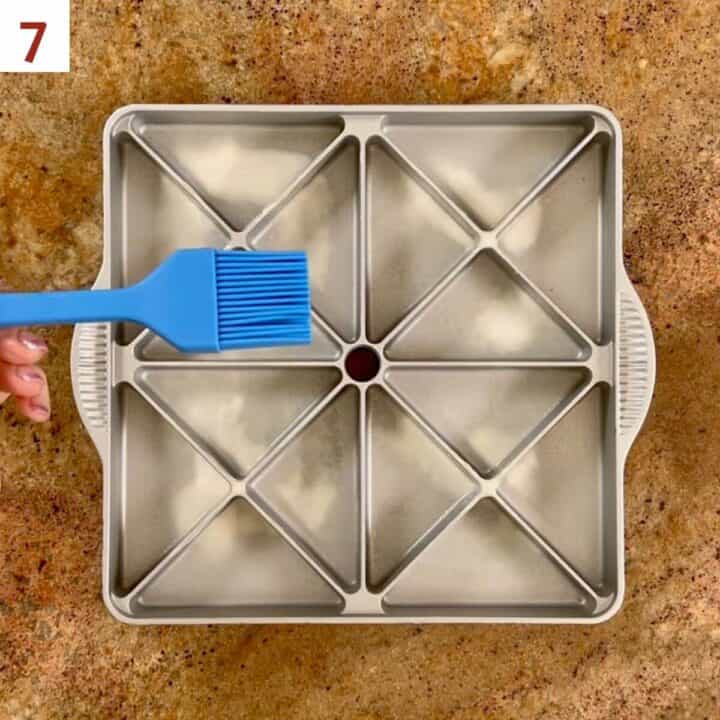 Brushing baking spray onto the wells of a mini scone pan.