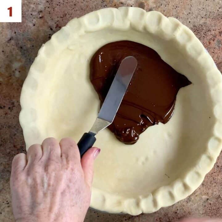 Spreading melted chocolate onto the bottom of the pie shell.